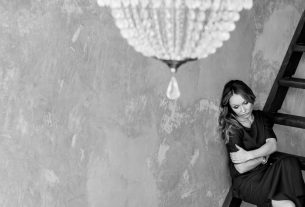 Black and white photo of a woman in an elegant dress under a chandelier.