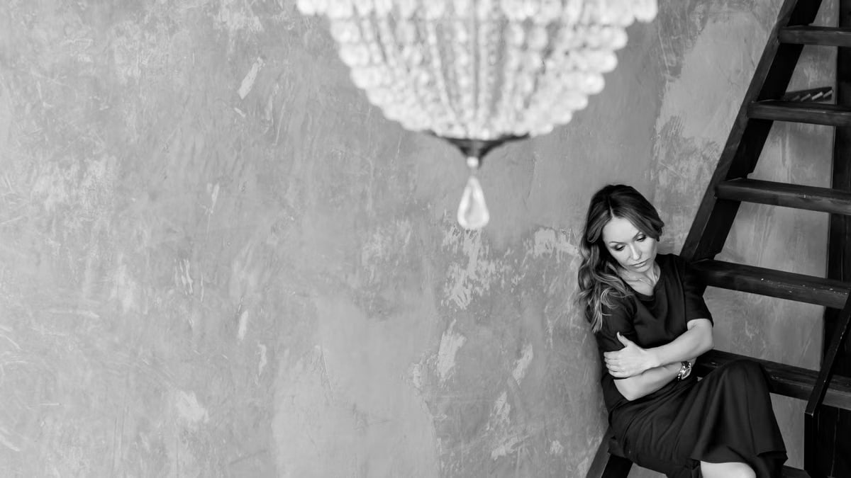 Black and white photo of a woman in an elegant dress under a chandelier.